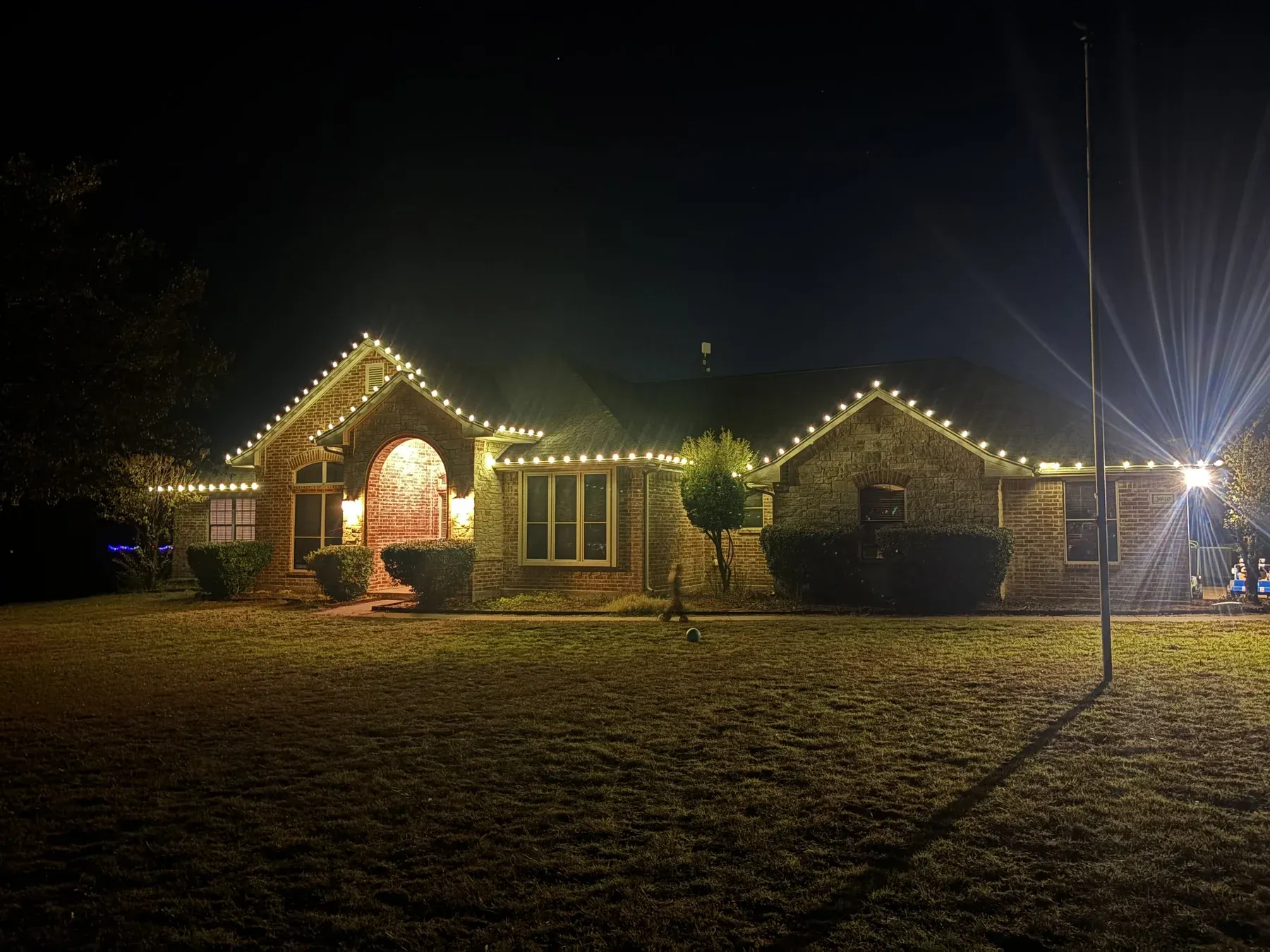 C9 roofline lights following the gables and arched entry of a stone and brick ranch home
