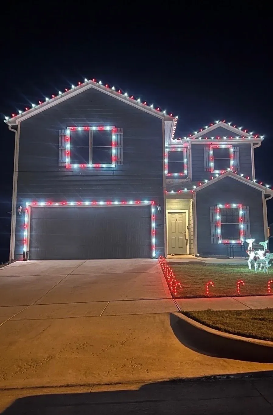 Red and white C9 lights outlining the roof, garage, and windows of a two story home with candy cane path lights